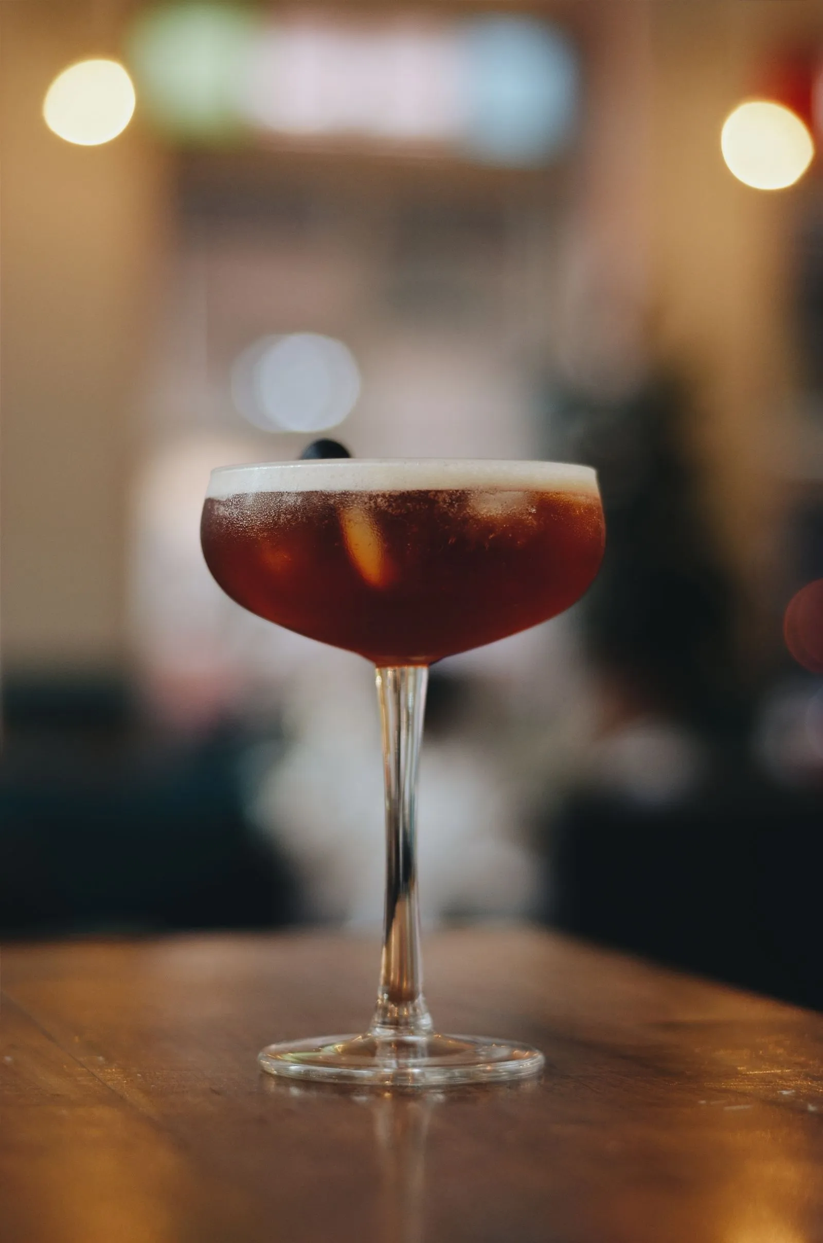 Donkere cocktail in coupeglas op een houten bar