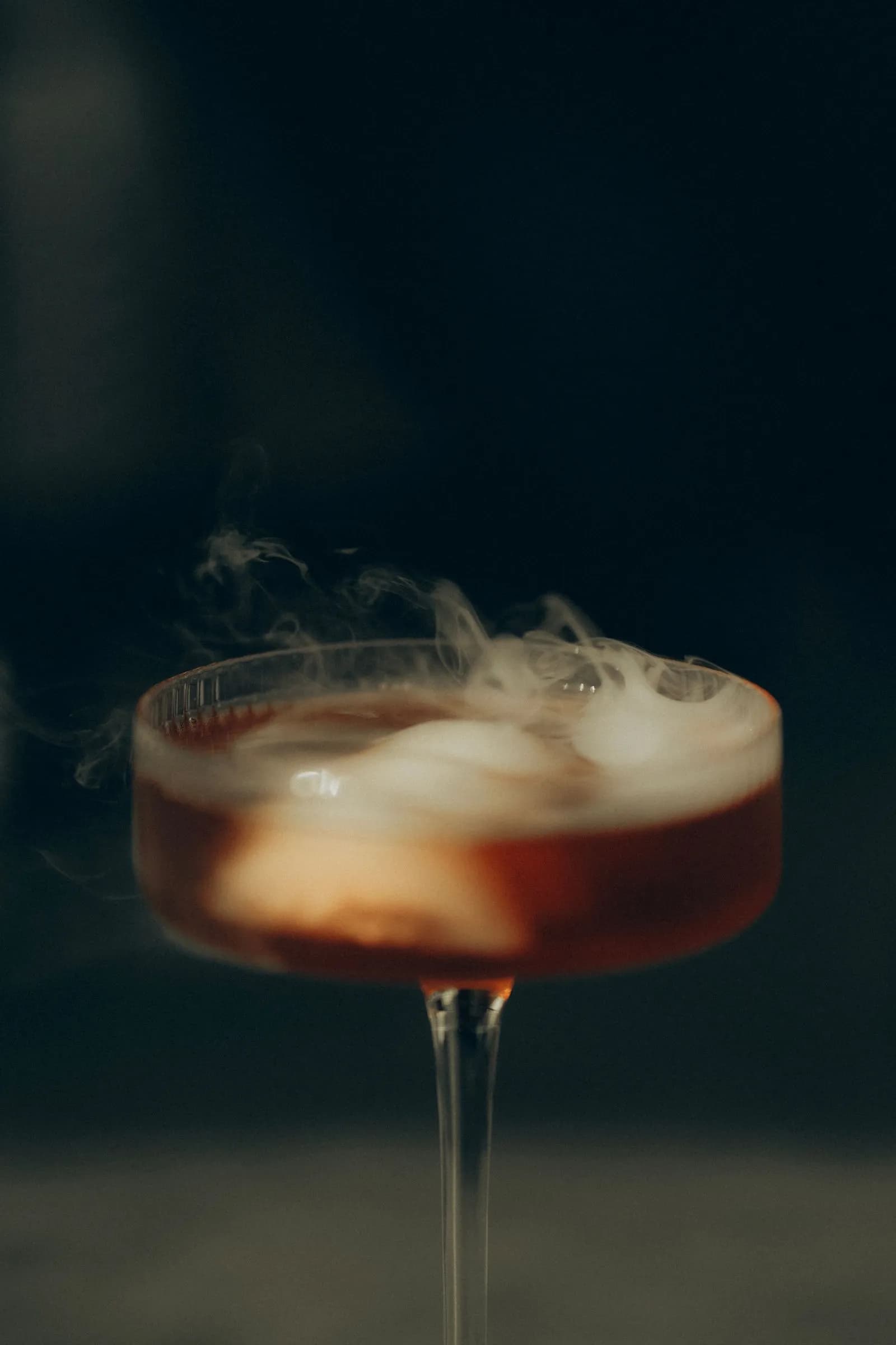 Rokende cocktail in een coupeglas op een donkere bar