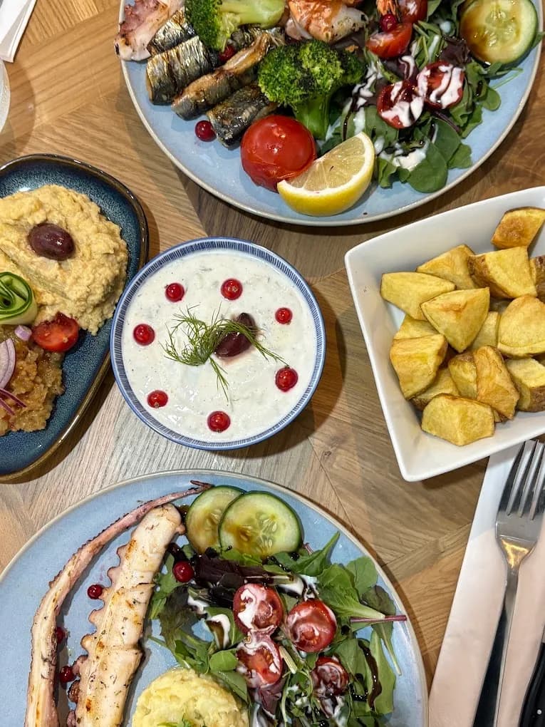Gedekte tafel van bovenaf met octopus, tzatziki, hummus, aardappelen en sardines